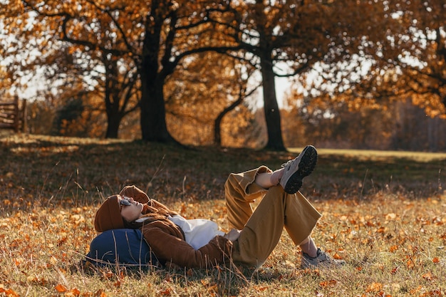 Side view of female backpacker lying on backpack and resting during hike in nature in fall season