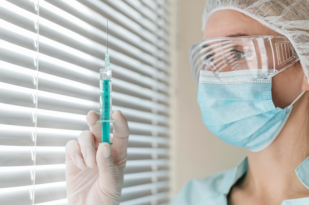 side view of female doctor with safety glasses and gloves holding syringe