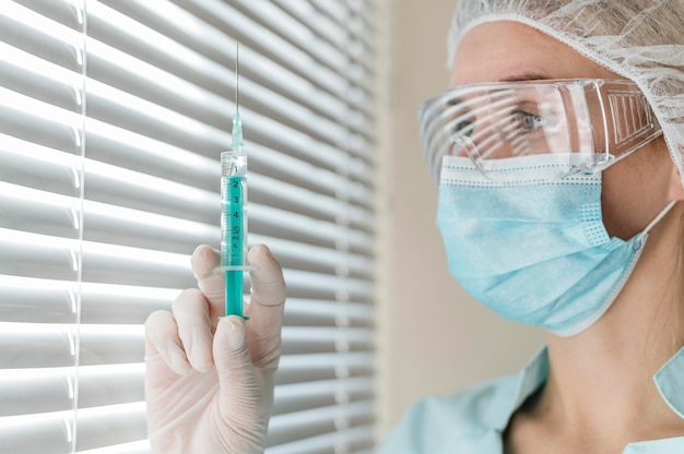 Side view of female doctor with safety glasses and gloves holding syringe