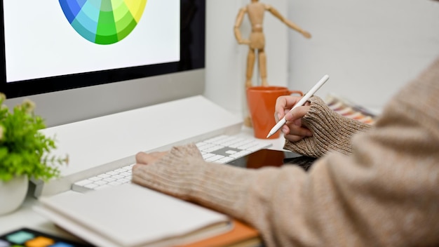 Photo side view of a female graphic designer working at her desk using computer and graphic tablet