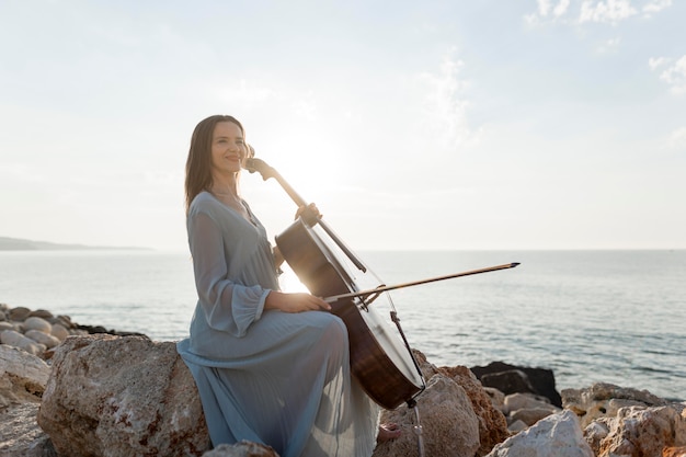 Foto vista laterale del musicista femminile che suona il violoncello in riva al mare sulle rocce