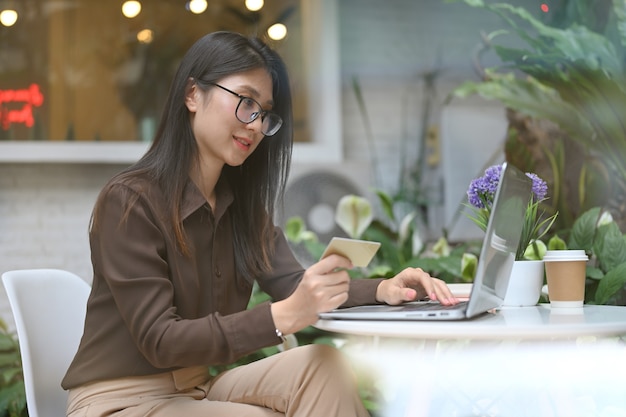 Vista laterale dell'impiegato femminile che fa operazioni bancarie in linea sul computer portatile mentre sedendosi nella caffetteria