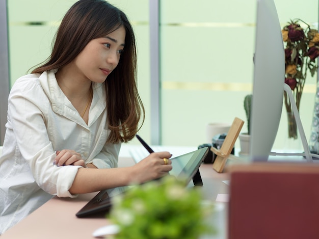 Side view of female office worker working on drawing tablet and computer in office room