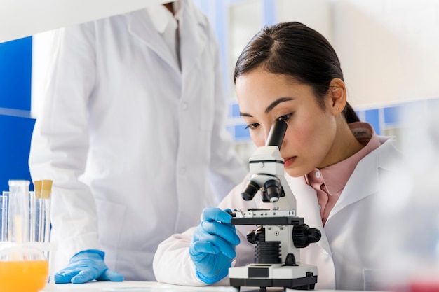 Foto vista laterale della scienziata in laboratorio usando il microscopio