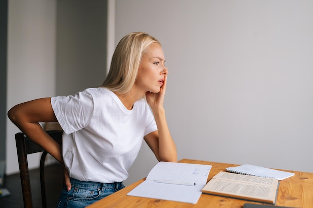 Side view of female student sit at desk touch back suffer from lower spinal spasm hurt unhealthy biracial woman stretch have strong backache