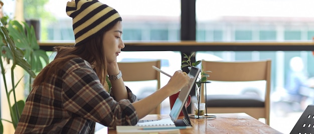 Side view of female teenager working with digital tablet on wooden table with coffee mug and plant vase