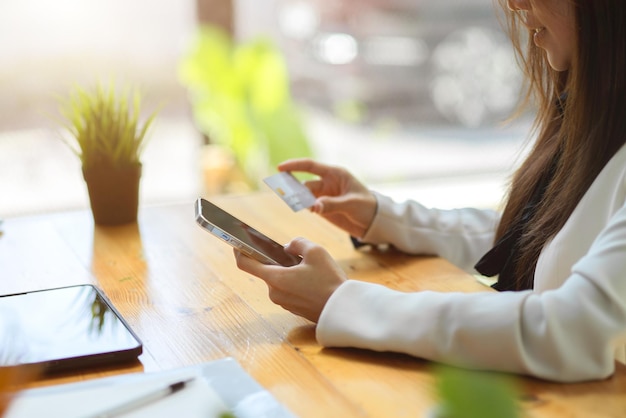 Side view A female worker holding a smartphone and credit or debit card over table online payment