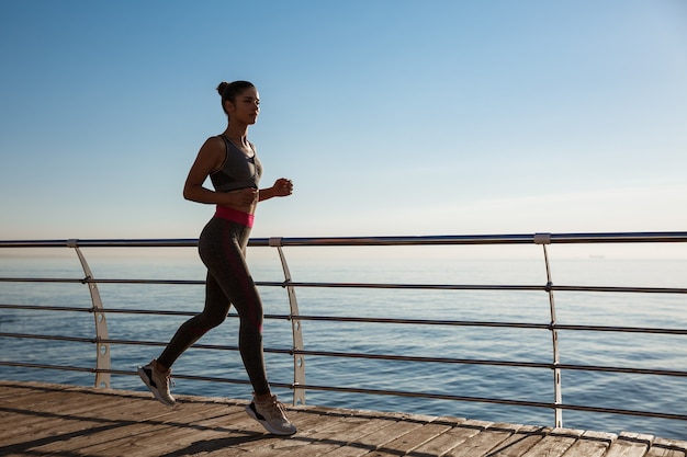 Side view of fitness woman running along seaside promenade