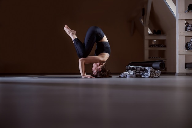 Вид сбоку гибкой подходящей женщины йога, балансирующей на голове. Интерьер студии йоги.