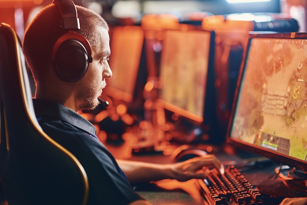 Side view of a focused male professional cybersport gamer wearing headphones looking at pc screen