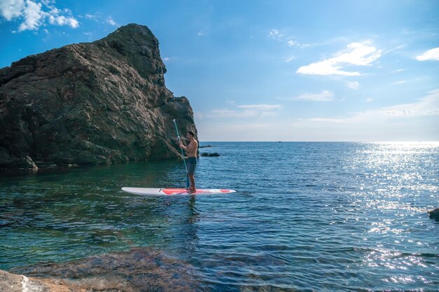 スタンドアップパドルボードで泳いだりリラックスしたりする男性の側面写真スタンドアップパドルボードで海に浮かぶスポーティーな男性SUP自然と調和したアクティブで健康的な生活のコンセプト