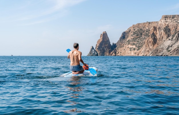 Side view foto of a man swiming and relaxing on the sup board sportive man in the sea on the stand