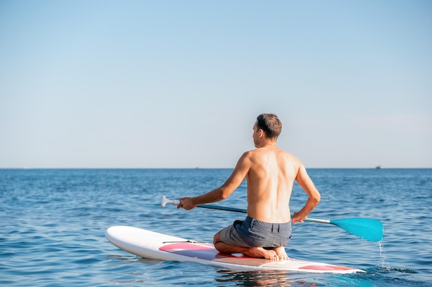 スタンドアップパドルボードで泳いでリラックスしている男性の側面写真スタンドアップパドルボードの海でスポーティーな男性