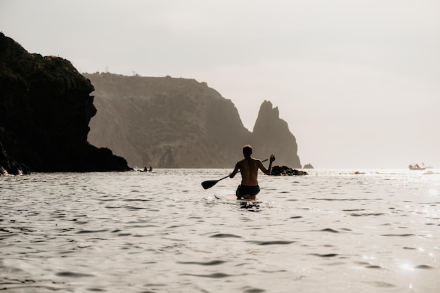 Side view foto of a man swiming and relaxing on the sup board sportive man in the sea on the stand