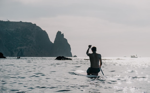 Side view foto of a man swiming and relaxing on the sup board sportive man in the sea on the stand