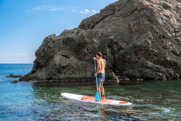 Side view foto of a man swiming and relaxing on the sup board sportive man in the sea on the stand