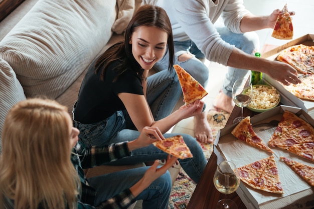 Photo side view of friends eating pizza in house