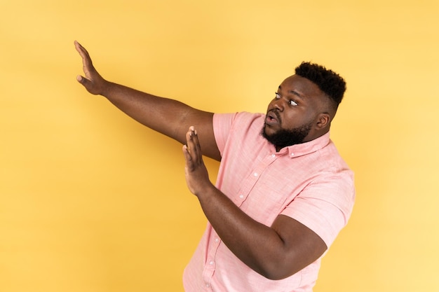 Side view of frightened man wearing pink shirt raising hands in fear looking horrified and panicking