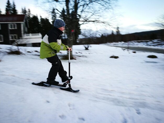 Боковой вид полной длины мальчика, едущего на скутере на покрытом снегом поле