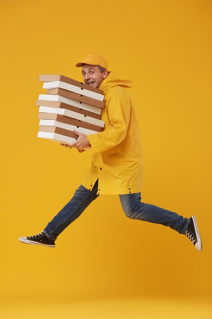 Side view full length of joyful delivery guy jumping high holding pizza boxes