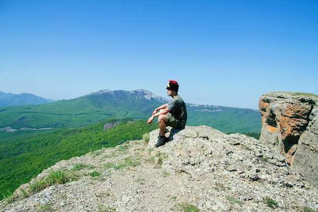 Photo side view full length of man sitting on mountain during sunny day