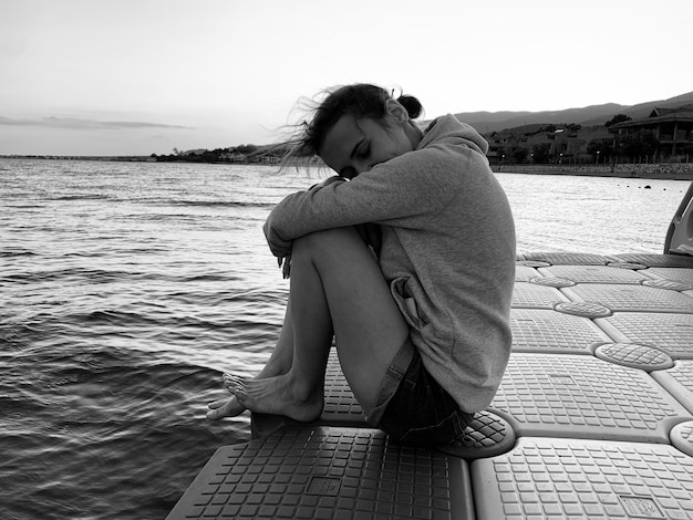 Foto vista laterale a tutta lunghezza di una giovane donna seduta sul mare sul molo