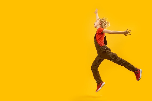 Side view fulllength portrait of bouncing boy on yellow background Child jumps happily Copy space place for text