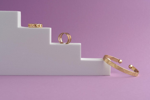 Side view of Geometric design bracelet and rings on white podium on pink background with copy space