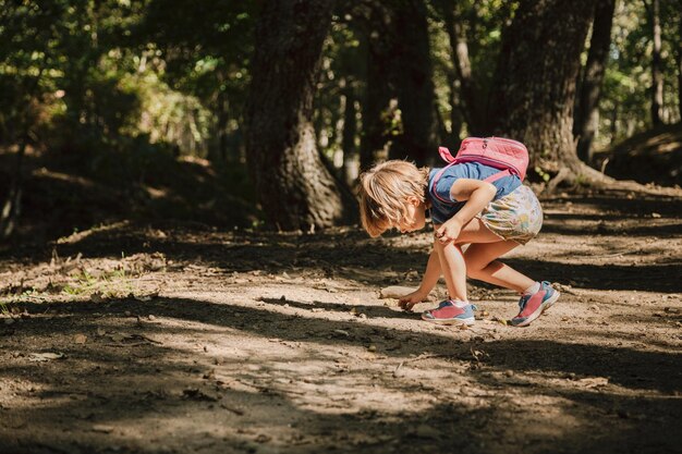 Foto vista laterale di una ragazza che raccoglie ghiande cadute sulla terra nella foresta