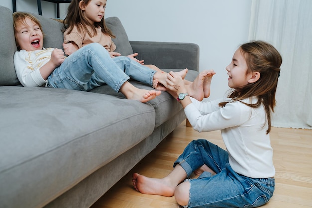 Side view of a girl conducting tickling competition between siblings sitting on a couch barefoot