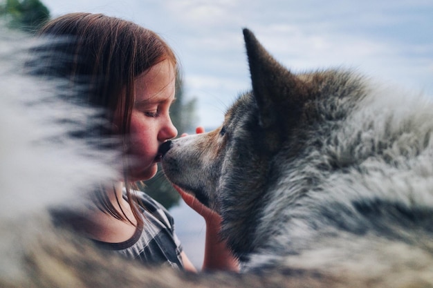 side view of girl kissing wolf against sky