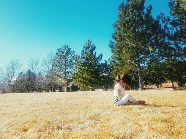 Photo side view of girl sitting at park during sunny day