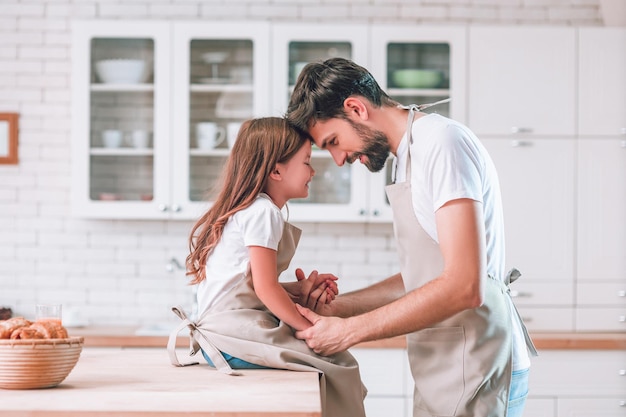 Side view of girl sitting on the table and father standing near in the kitchen looking at each other