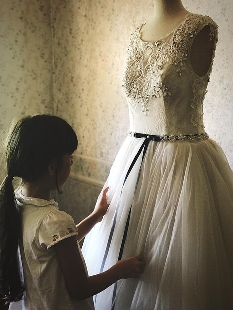 Photo side view of girl touching wedding dress on mannequin in store