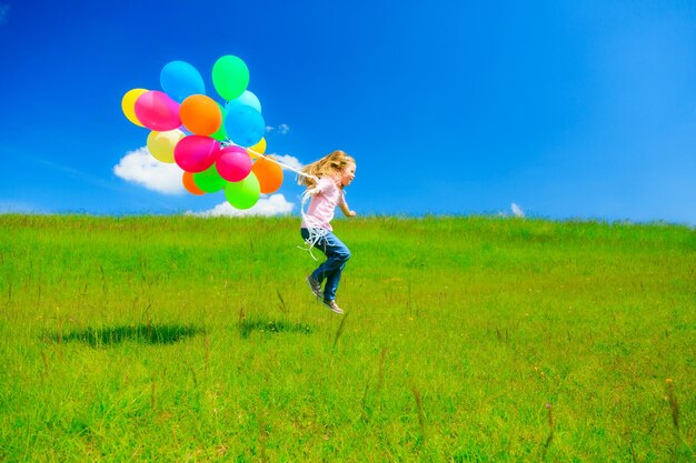 Side view of girl with colorful balloons jumping against sky