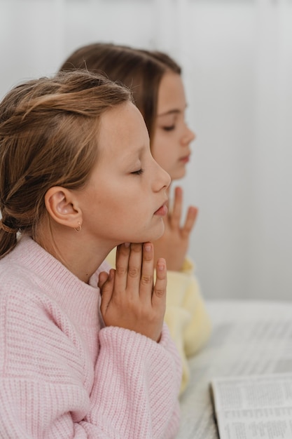 Photo side view of girls praying at home