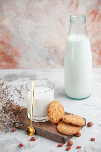 Side view of glass cup and bottle filled with milk cookies on the wooden board flower on mixed colors surface