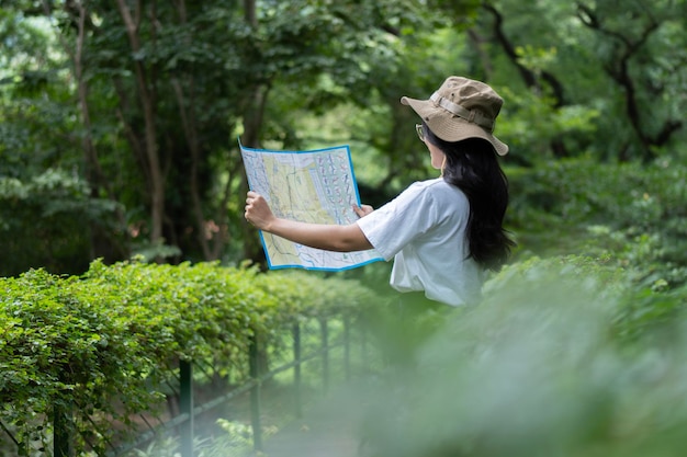 Photo side view of glasses girl holding a map tourist in the forest