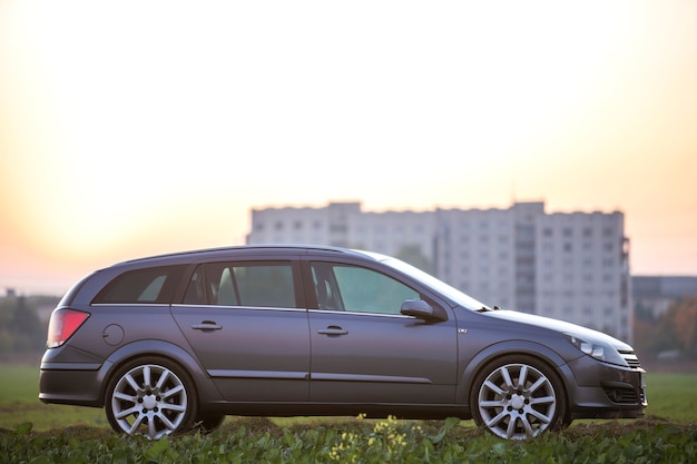 Side view of gray silver empty car parked in countryside on blurred rural landscape and bright orange clear sky at sunset copy space background. Transportation, traveling, vehicles design concept.