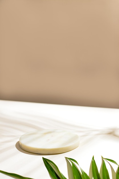 Photo side view green tropical palm leaf and white murble podium still life with sunlight and harsh shadow white empty table and beige wall minimal summer concept with palm leaf and shadow