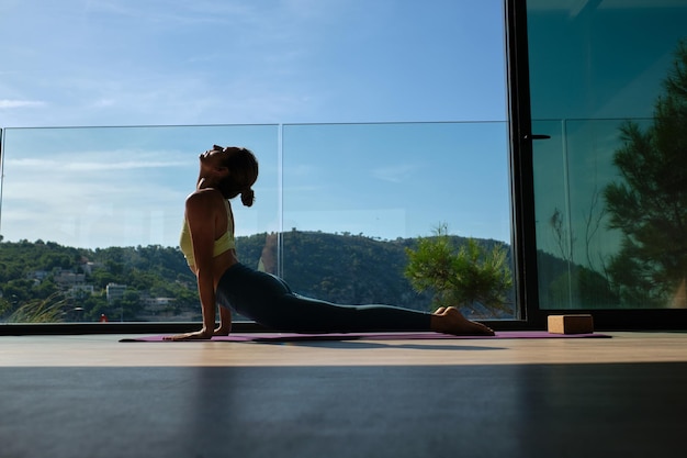 Side view ground level of slender female in Bhujangasana stretching body on mat while practicing yoga at home