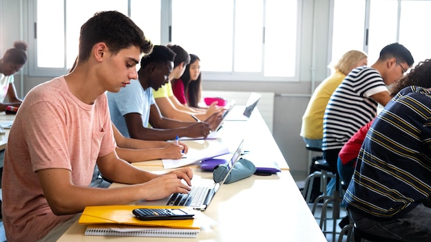 Photo side view of group of multiracial high school students studying and using laptops in class