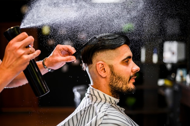 Side view hairstylist spraying his client's hair