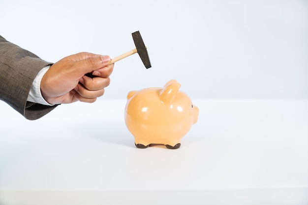 Side view of a hand with a hammer breaking a ceramic piggy bank with a white background and very good light