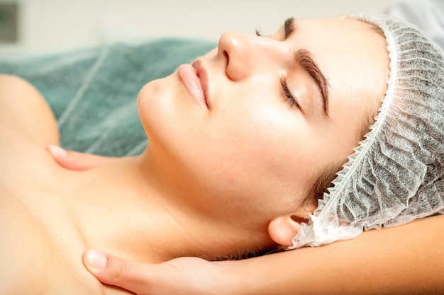 Side view hands of female therapist making massage of neck and shoulders to young caucasian woman in spa beauty salon