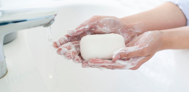 Photo side view of hands using bar of soap to wash