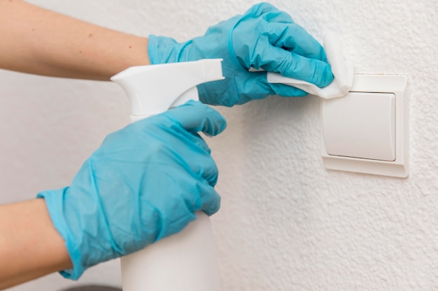 Foto vista laterale delle mani con guanti chirurgici che disinfettano l'interruttore della luce