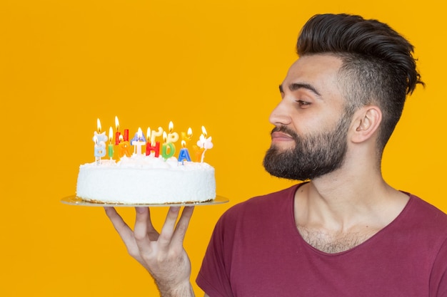 Vista laterale di un bel giovane barbuto arabo che spegne le candeline con una torta di congratulazioni in posa