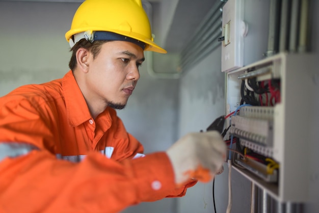 Side view of a handsome Asian electrician repairing an electrical box with pliers in the corridor