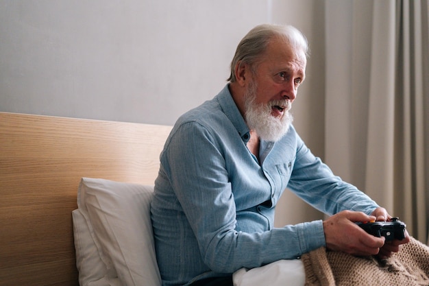 Side view of handsome grayhaired senior male playing online video game using gamepad at home having fun alone